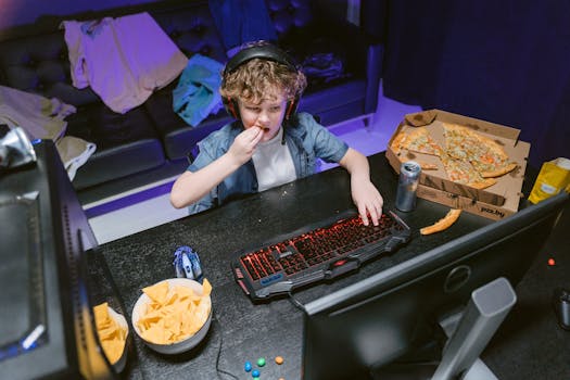 Boy playing video games with snacks and pizza by his side, enjoying leisure time.