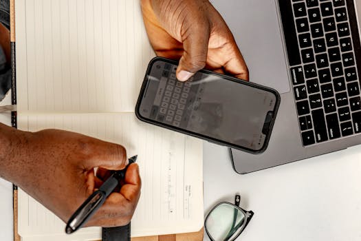 Business person multitasking with a smartphone and notebook at their desk.