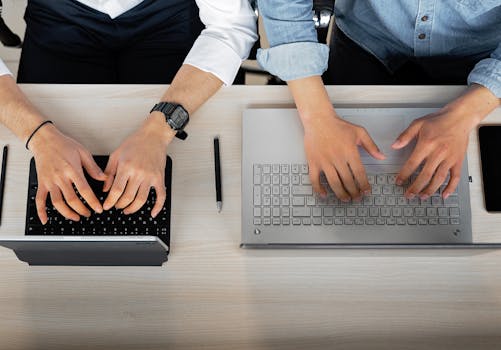 Two people working together with laptops and tablets at a modern workspace.