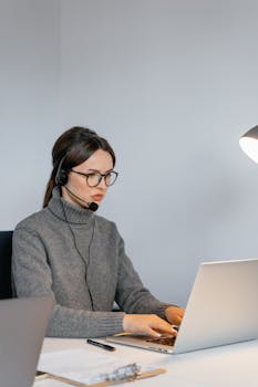 Focused woman in office with headset, providing customer support on laptop.