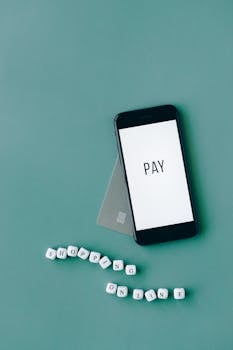 Minimalist flat lay of a smartphone with 'PAY' screen and payment card on a green background, emphasizing online shopping.