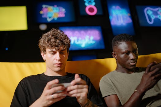 Two friends play mobile games indoors, focusing intently on their smartphones.